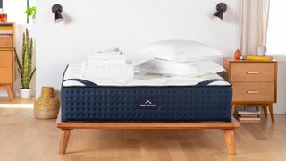 The DreamCloud Hybrid Mattress shown on a light wooden bed frame and covered in white pillows