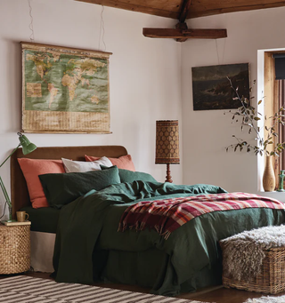 A warm and natural room with fern green bedding that is mixed with terracotta and red throws and pillows. There is a map hanging above the bed and a brown headboard.