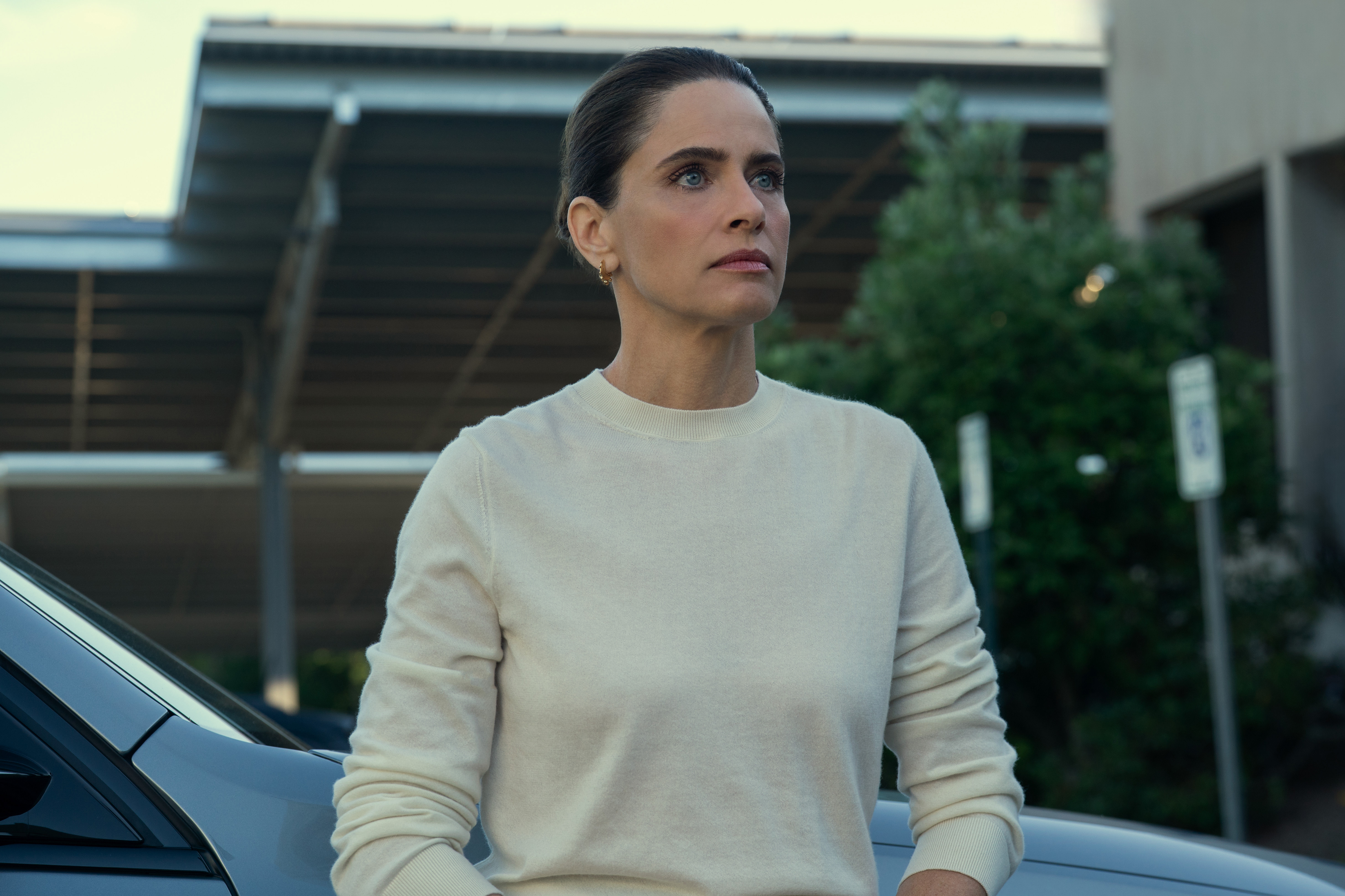 amanda peet as mel cooper wearing a white longsleeve top and walking outside in your friends and neighbors season 2