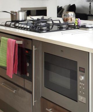 A white kitchen island with two silver ovens built into the base and a black hob with a silver saucepan on top