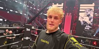 Jake Paul with a Team Paul black shirt on inside a boxing ring looking happy.
