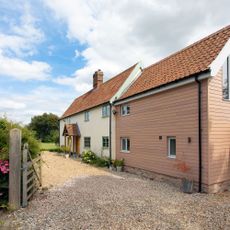 Gravel driveway in front of cottage style home with cladding and a porch