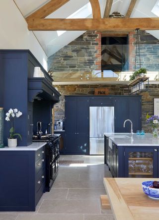 blue open plan kitchen with large kitchen island in double height space with exposed beams