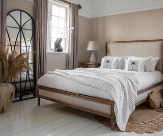 cream and wooden bed with black arched mirror leaning against one wall