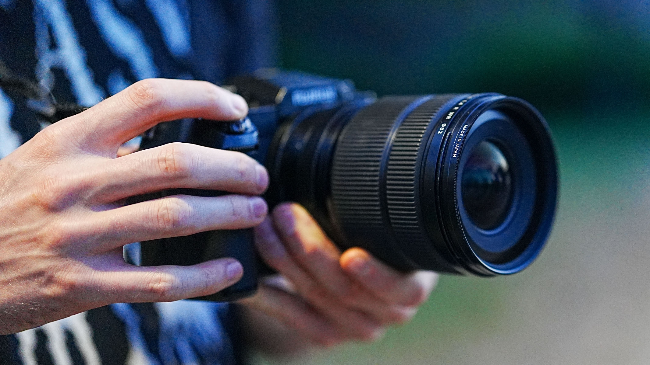 A close-up of hands holding the Fujifilm GFX100S II with the Fujifilm GF 20-35mm f/4 R WR lens attached.