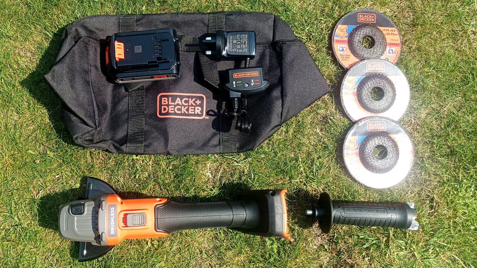 Top-down shot of the contents of Black + Decker Cordless Brushless Angle Grinder set on grass