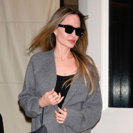 Angelina Jolie in New York City on December 2, 2024 wearing a gray cardigan, black dress, and black Celine platform slide sandals.