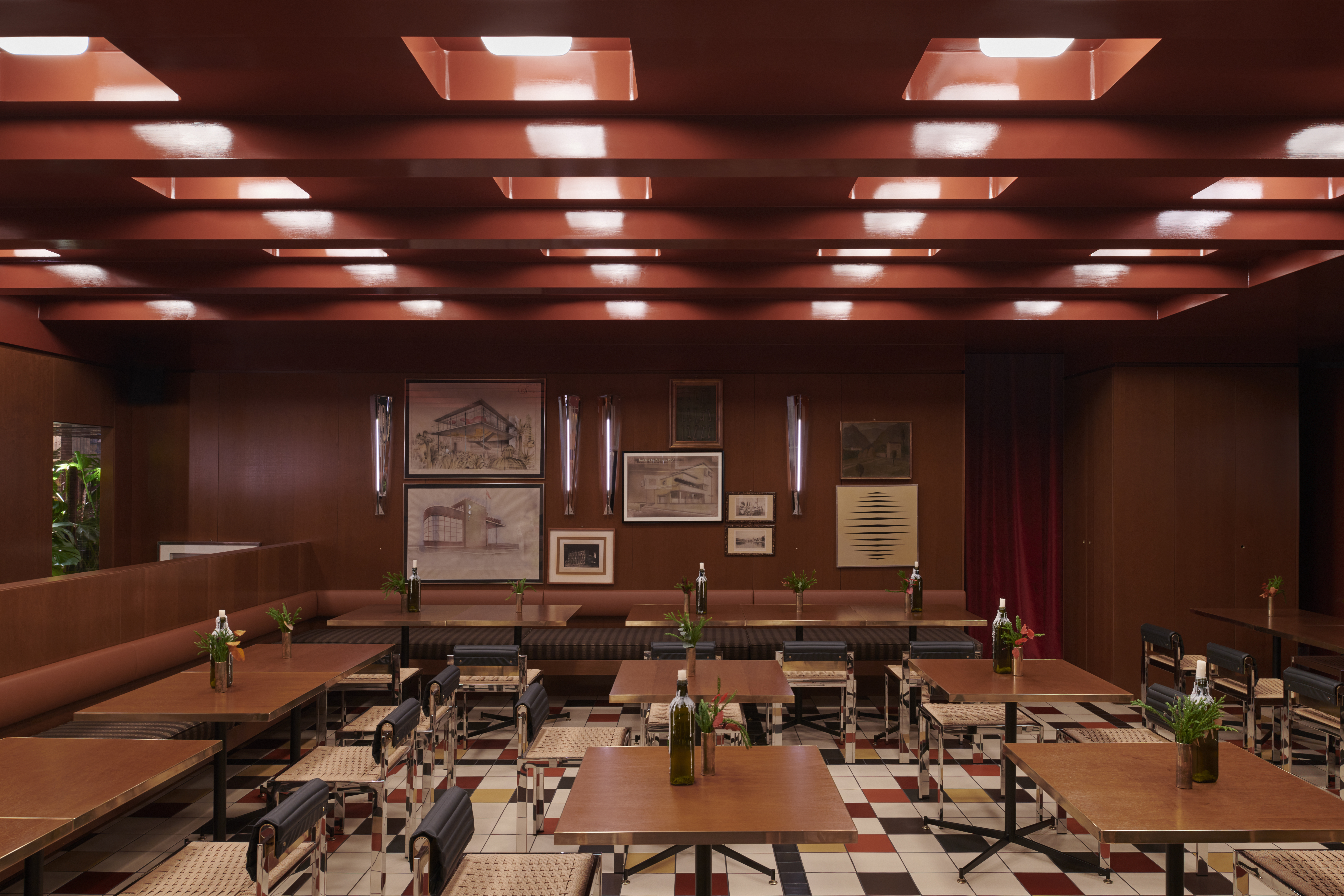 A restaurant&#039;s dining room boasts back-lit coffered ceilings, mid-century furniture in leather, chrome, and wood, framed artworks scattered across its walls, checkered floors, and a downstairs bar clad in brushed steel and golden light.
