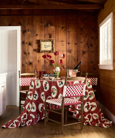 Rustic, wood-paneled holiday dining room featuring a burgundy block-printed tablecloth, green vase of anthuriums, and eclectic goblets