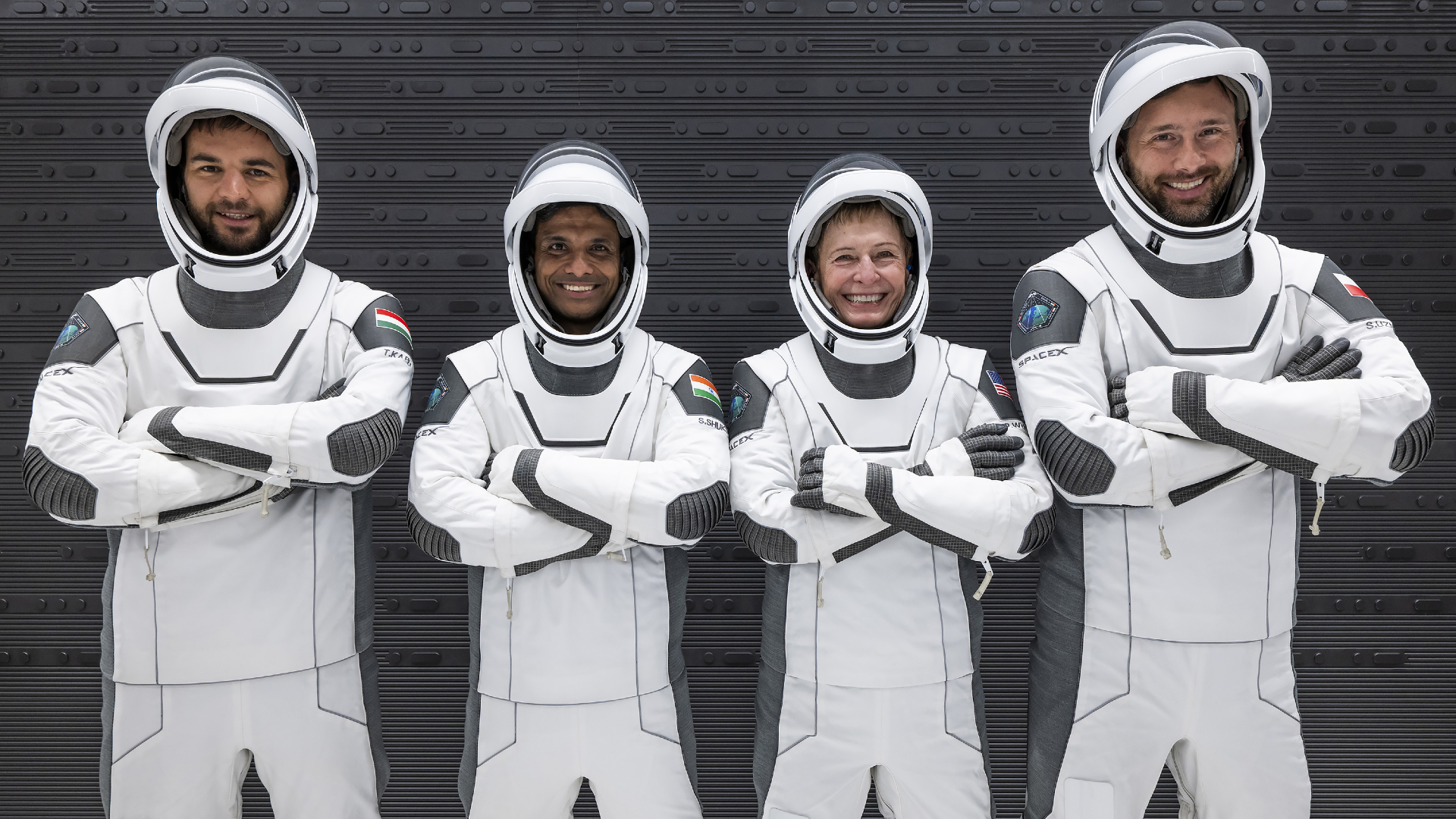 portrait of four astronauts — three men and one woman — in black and white spacesuits