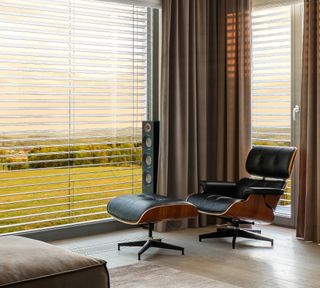 Eames lounge chair and footstool in front of a window with blinds