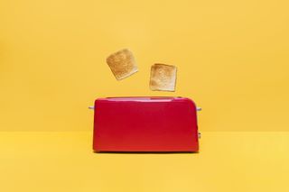 Front view of red toaster toasting two bread slices on yellow background.