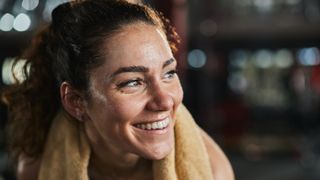 Woman happy with sweaty face and towel around her shoulders at the gym