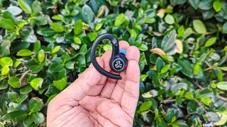 JLab Epic Air ANC 2 earbuds held in hand against a green leafy background