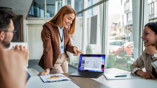 Dell Pro laptop shown being used in a presentation to multiple people sat around a desk
