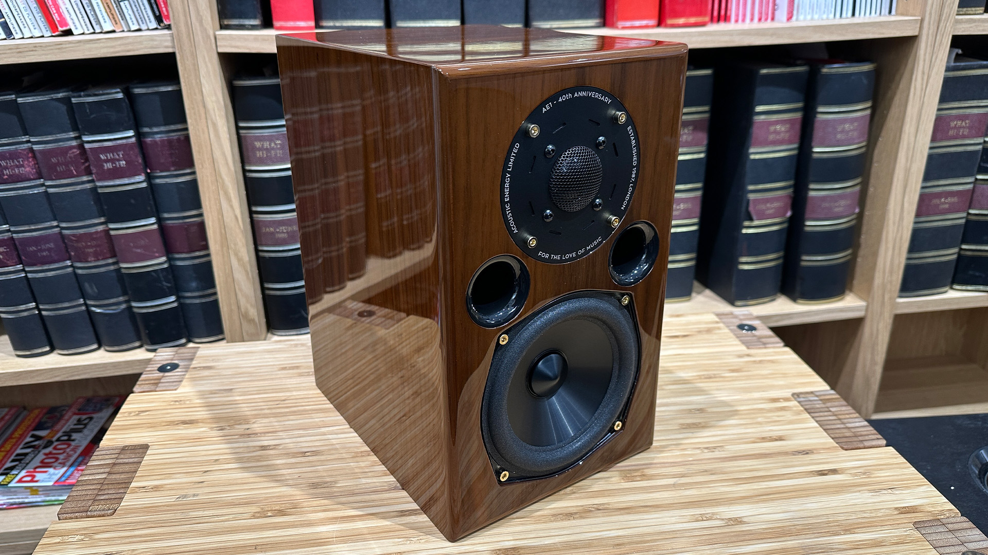 Acoustic Energy AE1 40th Anniversary standmount speaker on wooden hi-fi rack in front of bookcase