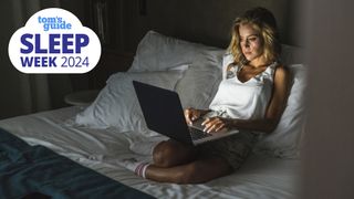 A woman with blonde hair makes the big nighttime routine mistake of working on her laptop in a dark bedroom close to bedtime