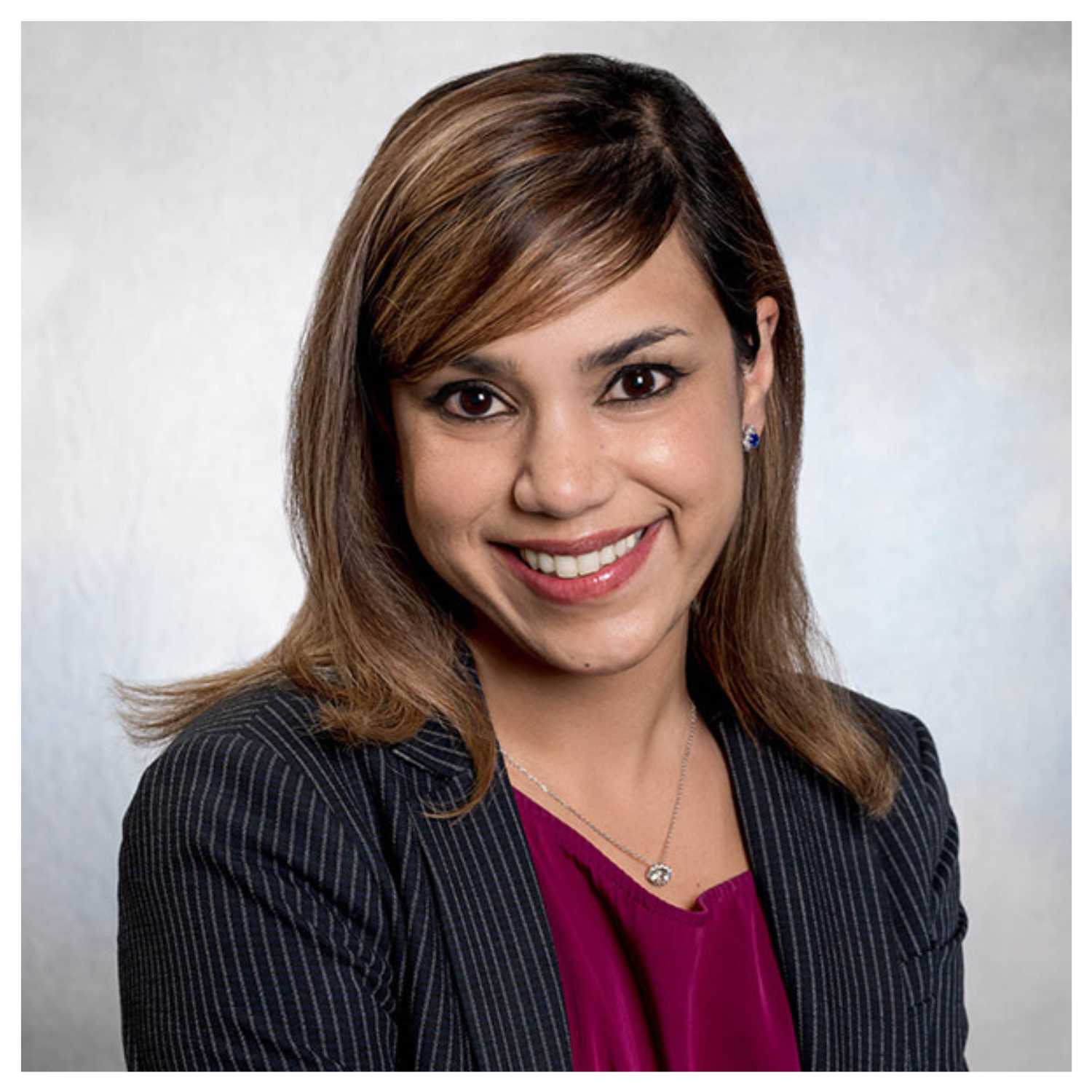 A headshot of a woman in a maroon blouse and a pinstripe blazer smiling