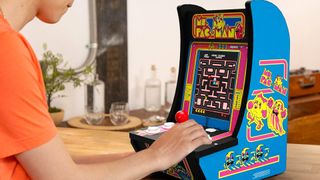 Player using Arcade1up Ms. Pac-Man arcade machine on wooden table