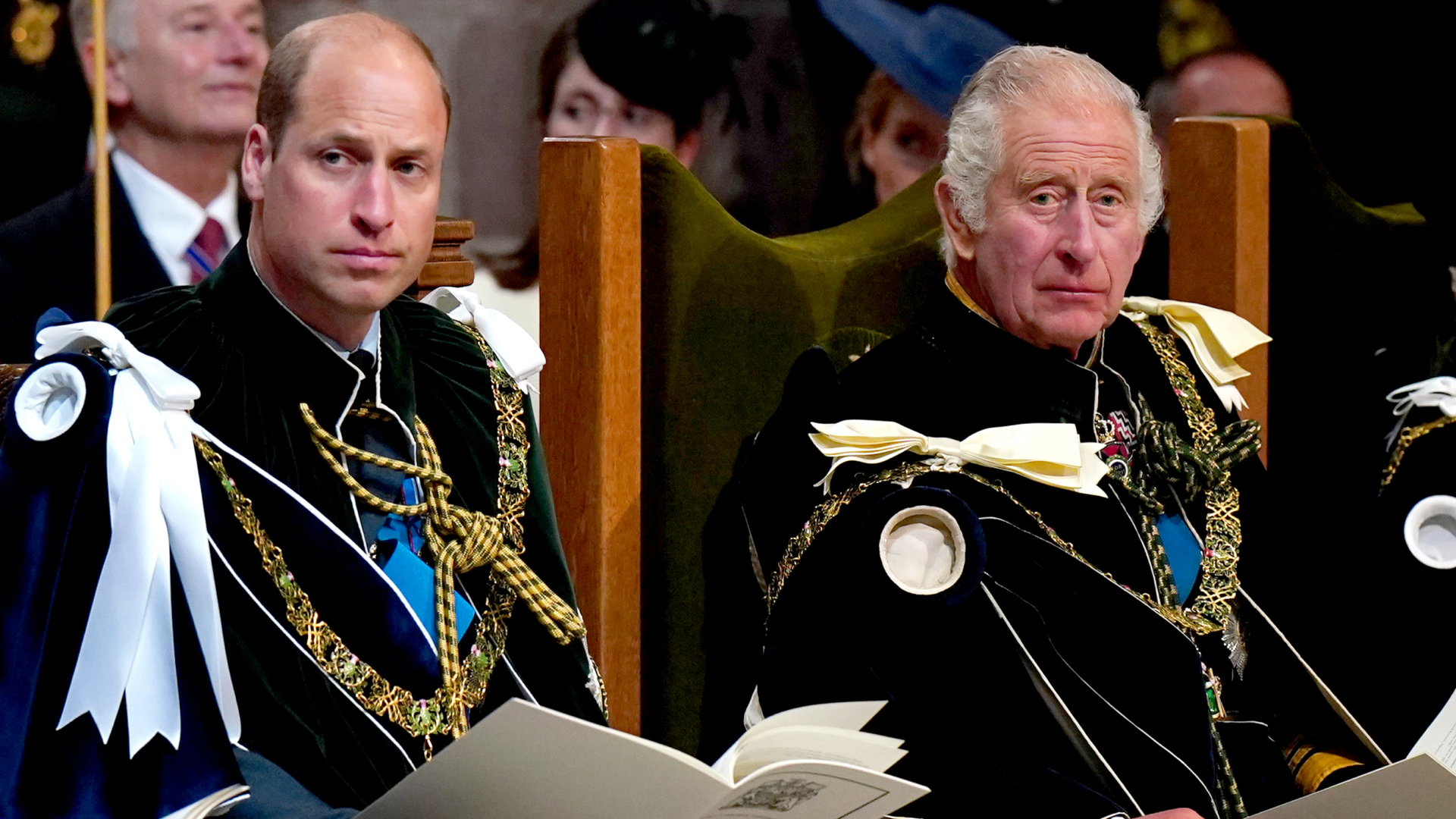 King Charles and Prince William wearing velvet robes sitting in chairs