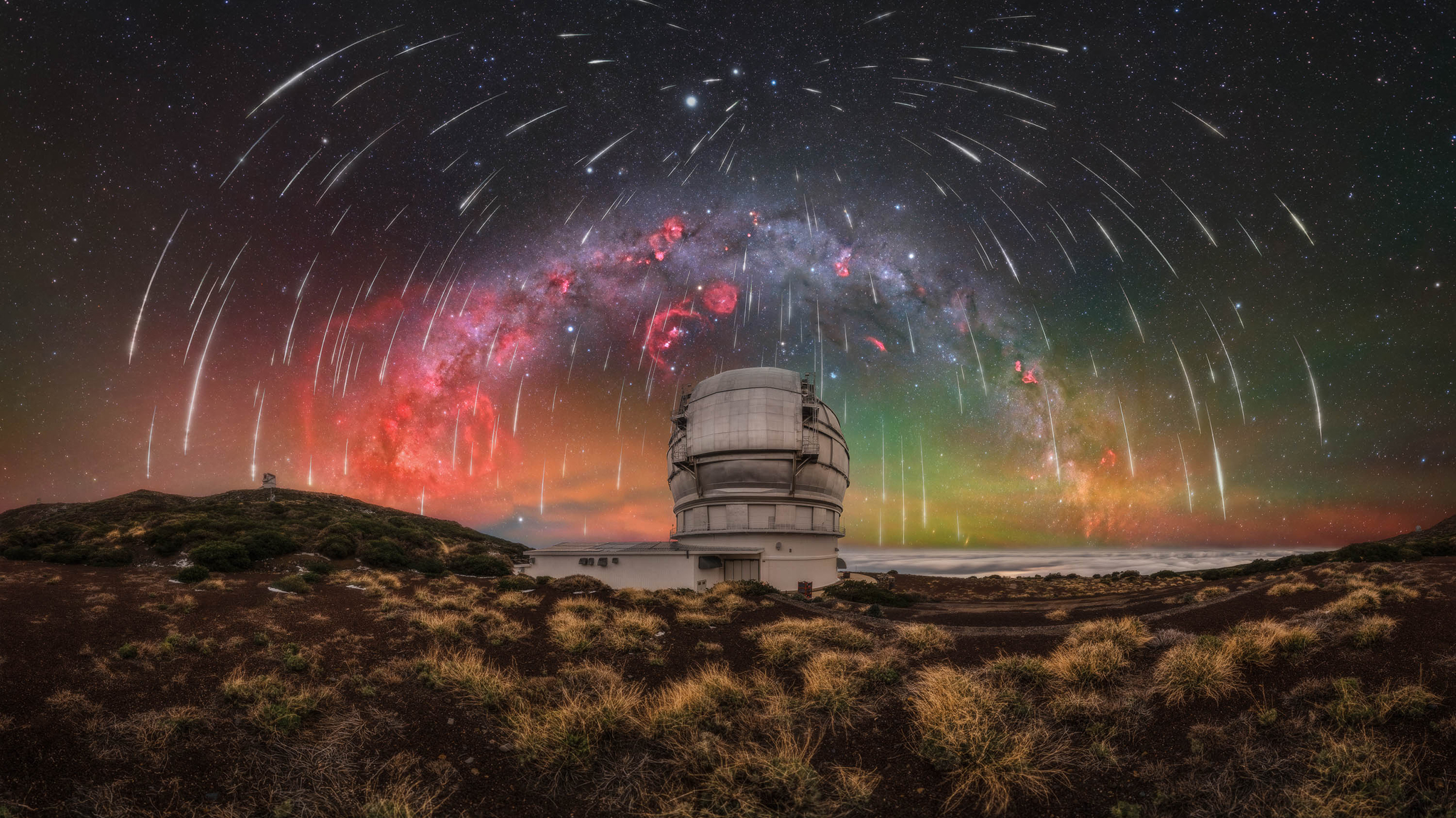 Observatory under a meteor shower with a colorful Milky Way arching across a starry night sky