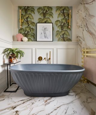 grey freestanding bath in bathroom with green floral wallpaper panel and marble tiling