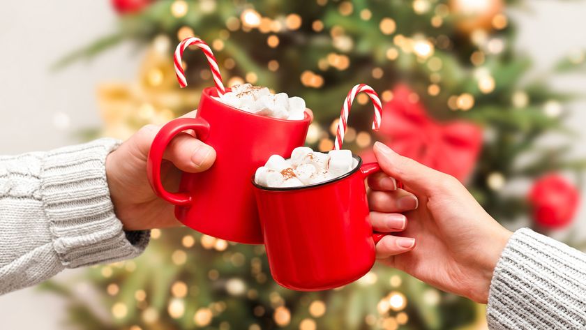 two red christmas espresso drinks mugs with candy canes and a christmas tree in the background and whipped cream and marshmallows