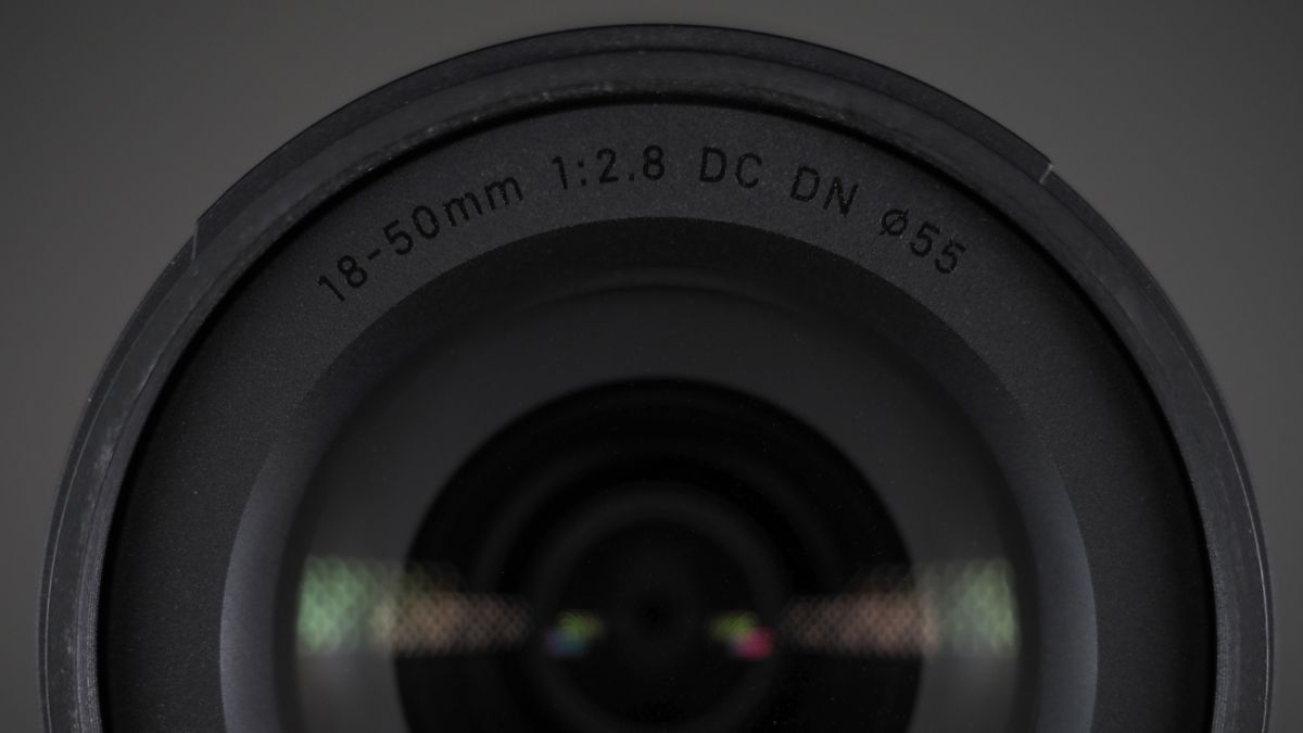 The Sigma 18-50mm f/2.8 DC DN | C Canon RF lens on a wooden surface against a dark background with moody lighting
