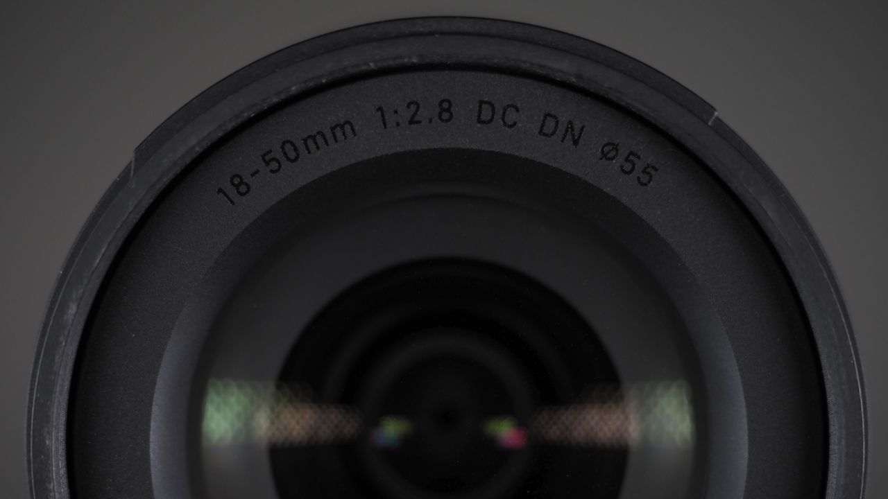 The Sigma 18-50mm f/2.8 DC DN | C Canon RF lens on a wooden surface against a dark background with moody lighting