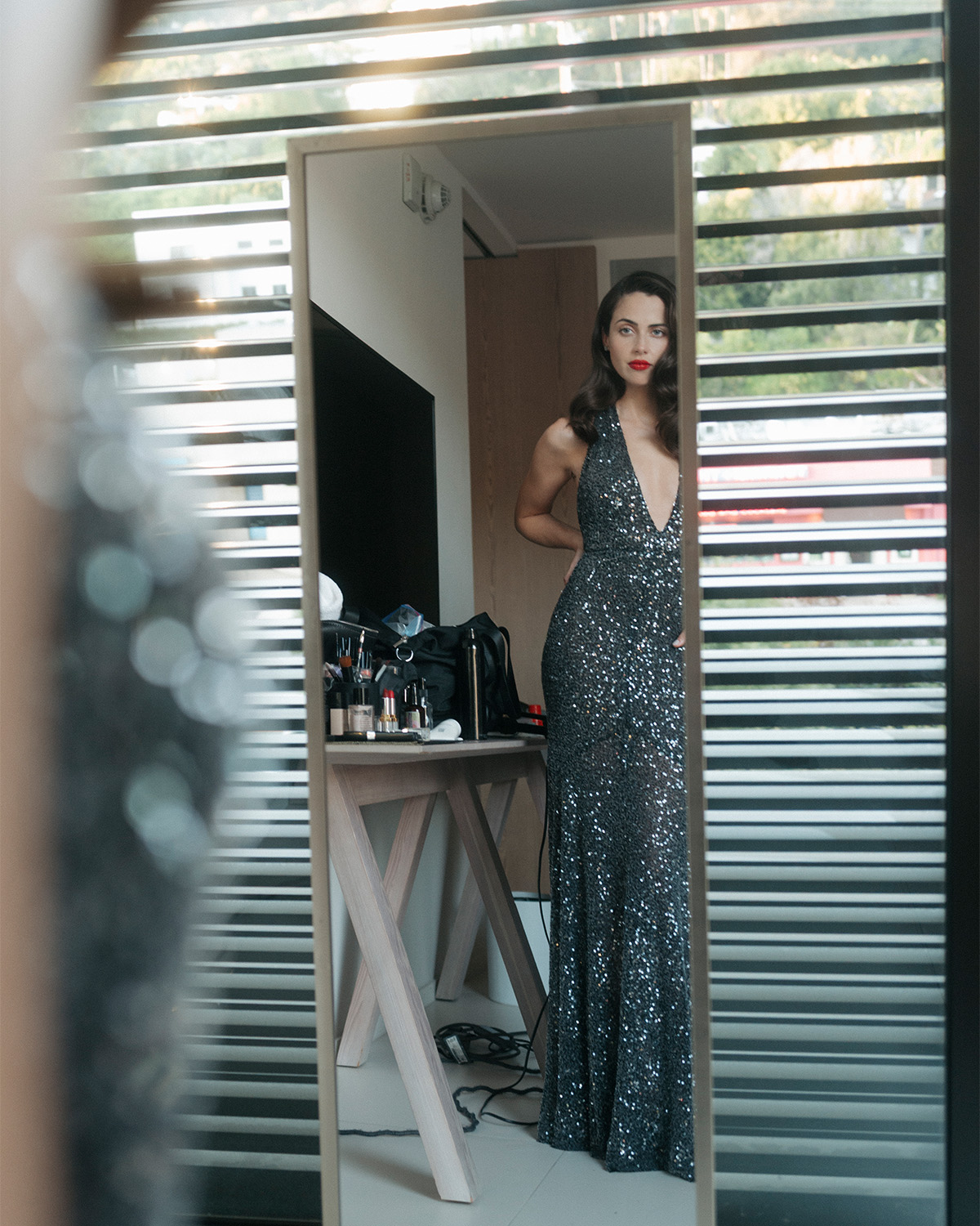Lydia Peckham looks at herself in the mirror before heading to the Nuremberg AFI Fest premiere. She is wearing a black sequin gown with plunging halter neckline.