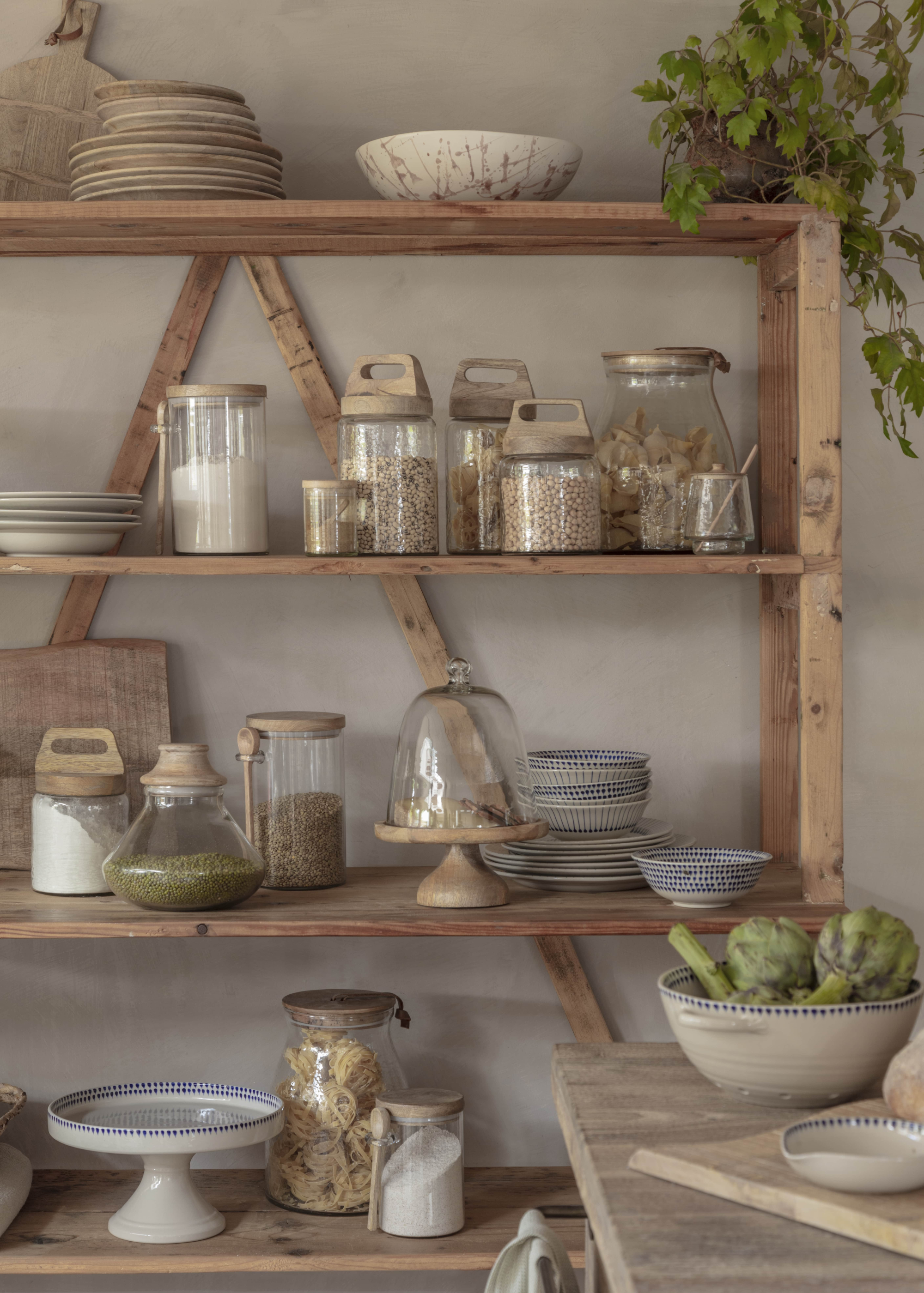 A rustic kitchen shelf with glass bottles of spices and cooking ingredients
