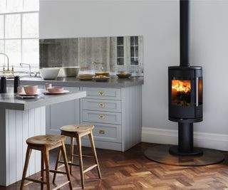 freestanding black log burner in kitchen with wooden herringbone flooring and grey kitchen with central island unit