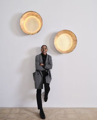 A portrait of designer Tiarra Bell alongside two wall lamps she designed, photographed at Carpenters Workshop Gallery