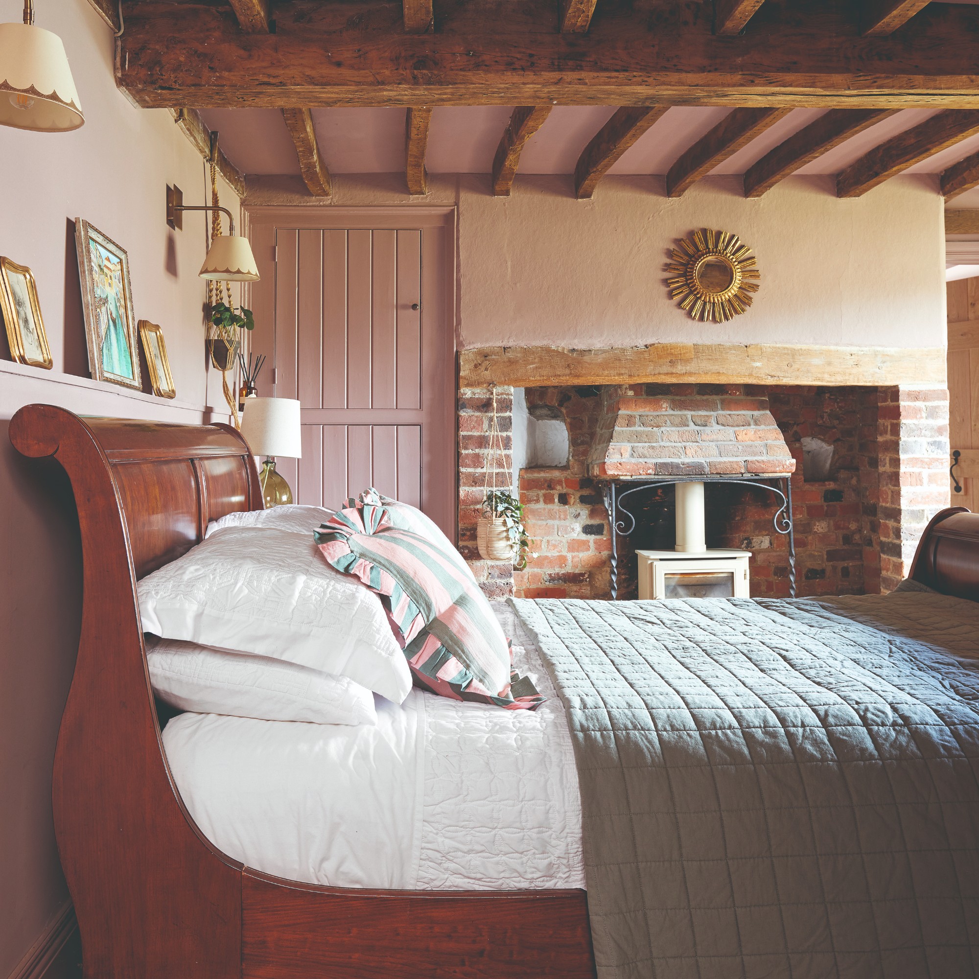 A soft pink-painted bedroom with exposed beams and a vintage dark wood bed frame