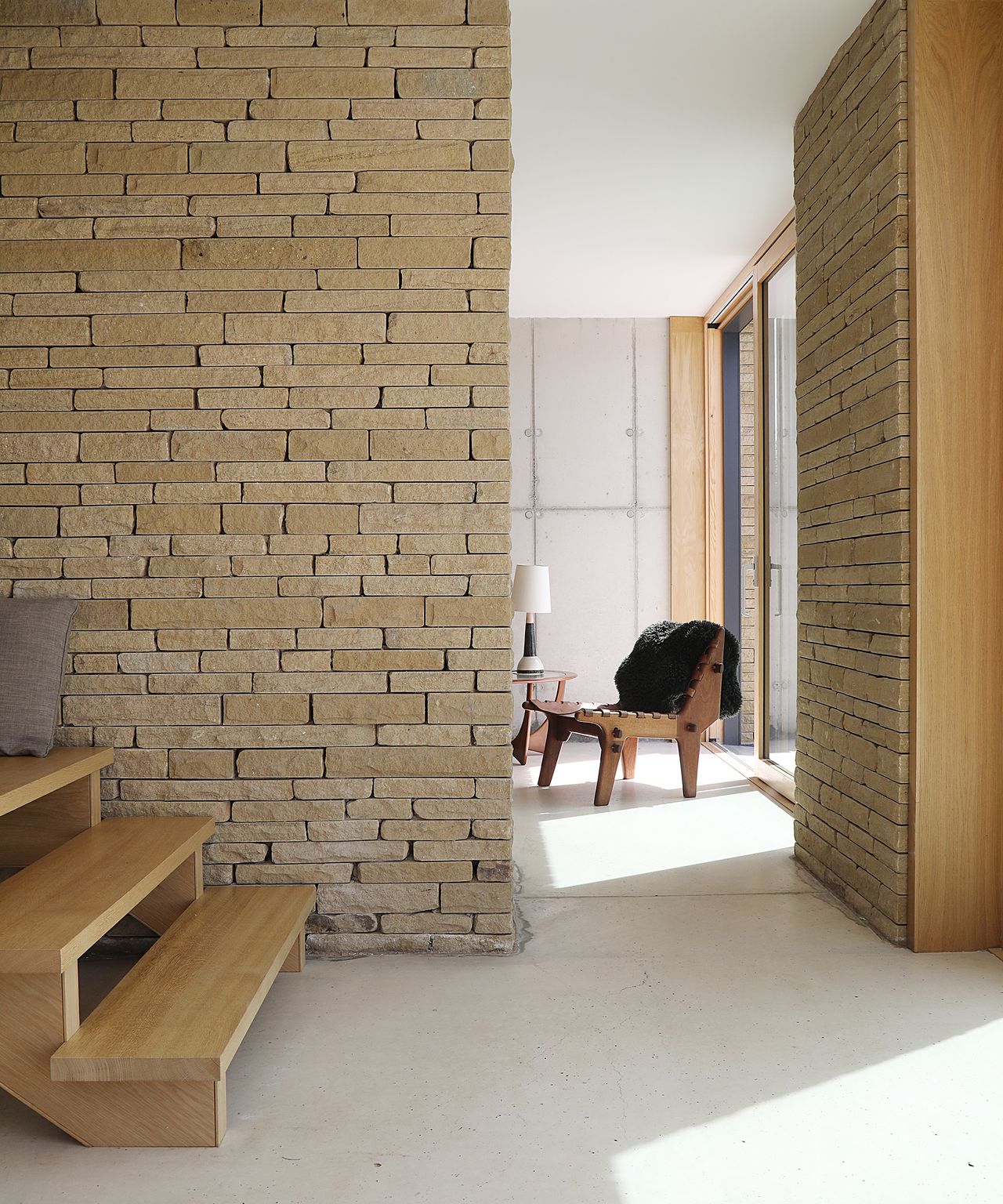View from a light coloured dining room/kitchen into a living room area. There are stairs to the left and exposed brick walls
