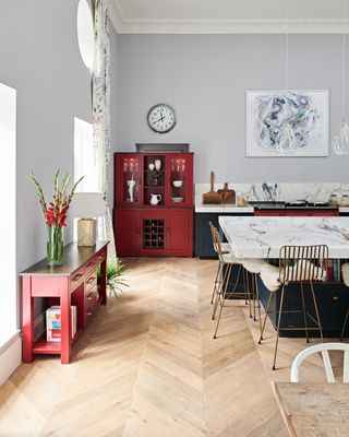 Pale gray painted kitchen with red kitchen cabinet, white marble counter tops and black dining chairs