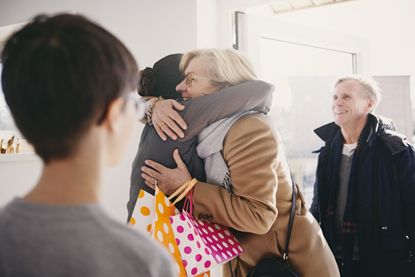 Older woman hugging daughter while standing at doorway with family