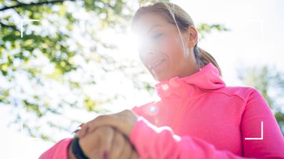 Woman looking down at a watch with sunlight coming through the trees behind her, representing working out as one of the best Apple Watch tips to follow