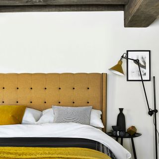 bedroom with white wall and bedding with yellow cushion and throw and bedside lamp