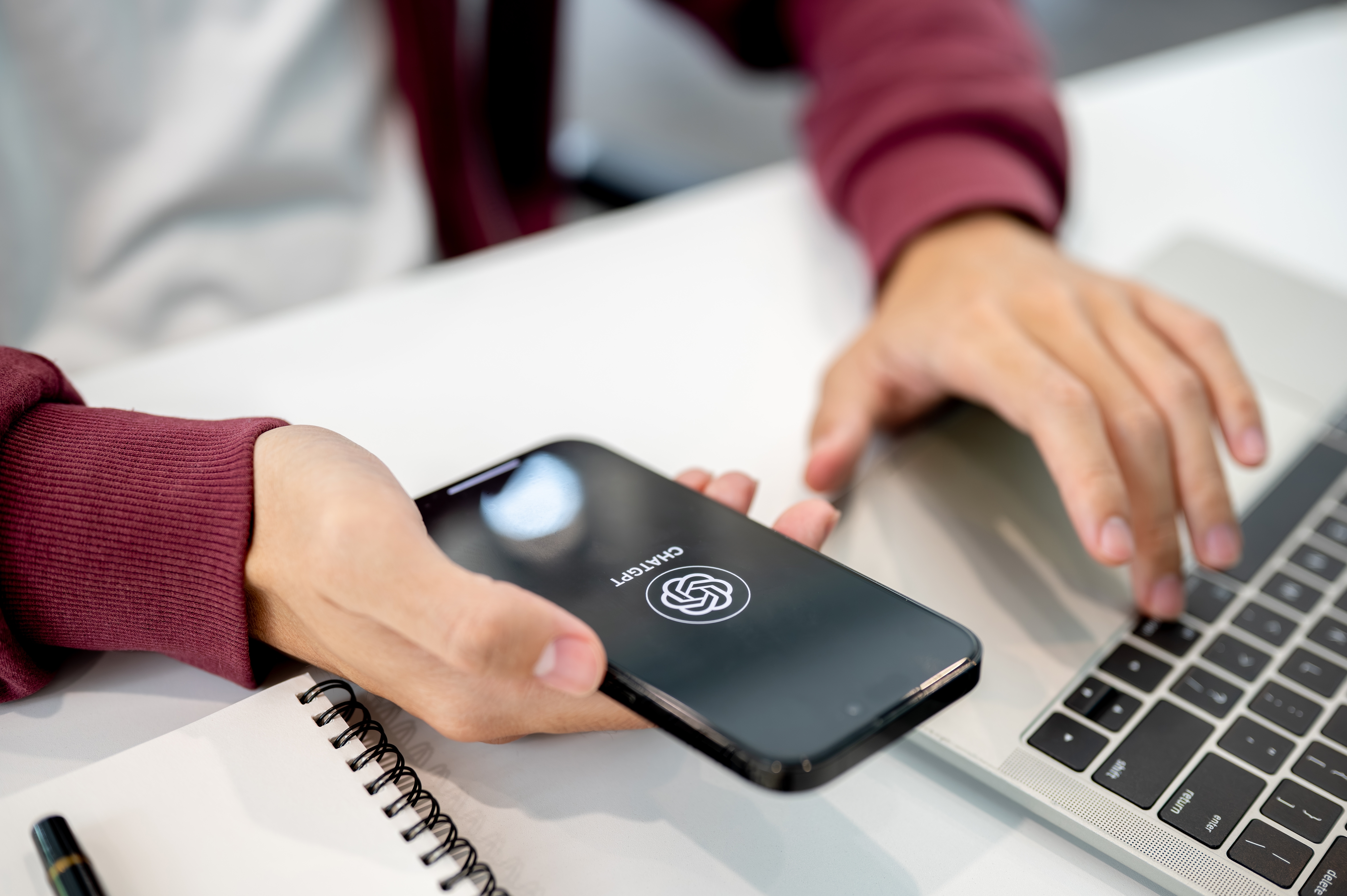 Man student holding phone with ChatGPT app aside laptop.