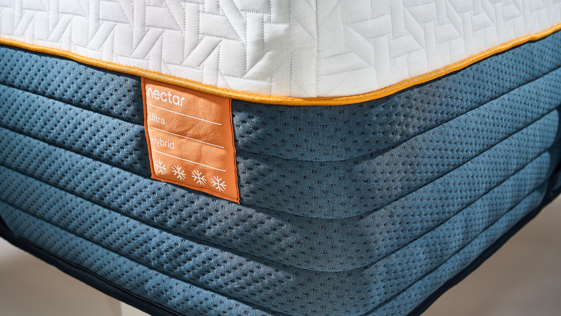 The square orange Nectar Ultra Hybrid label sewn onto the side of the mattress showing the the model name and four snowflakes to signify the cooling technology