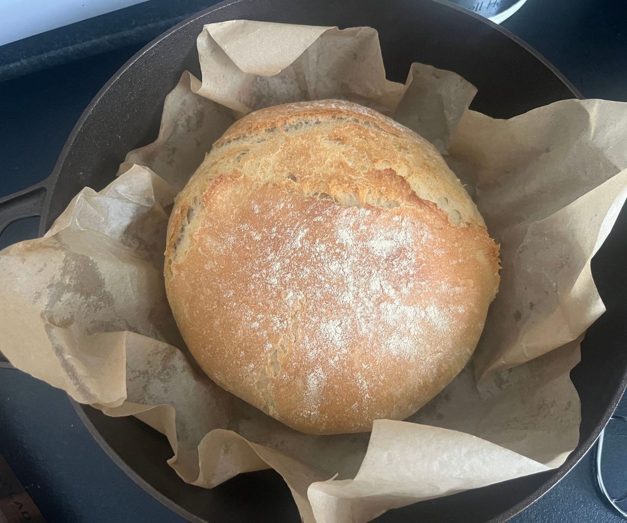A load of round rustic bread nestled in baking paper inside a cast-iron Dutch oven.