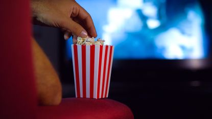 Small bucket of popcorn resting on the arm of a chair in the cinema