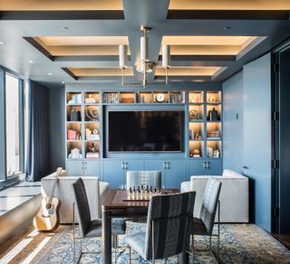 blue games room with tv integrated into the shelving, gray armchairs, games table with chess board and four dining chairs, guitar, rug, lighting