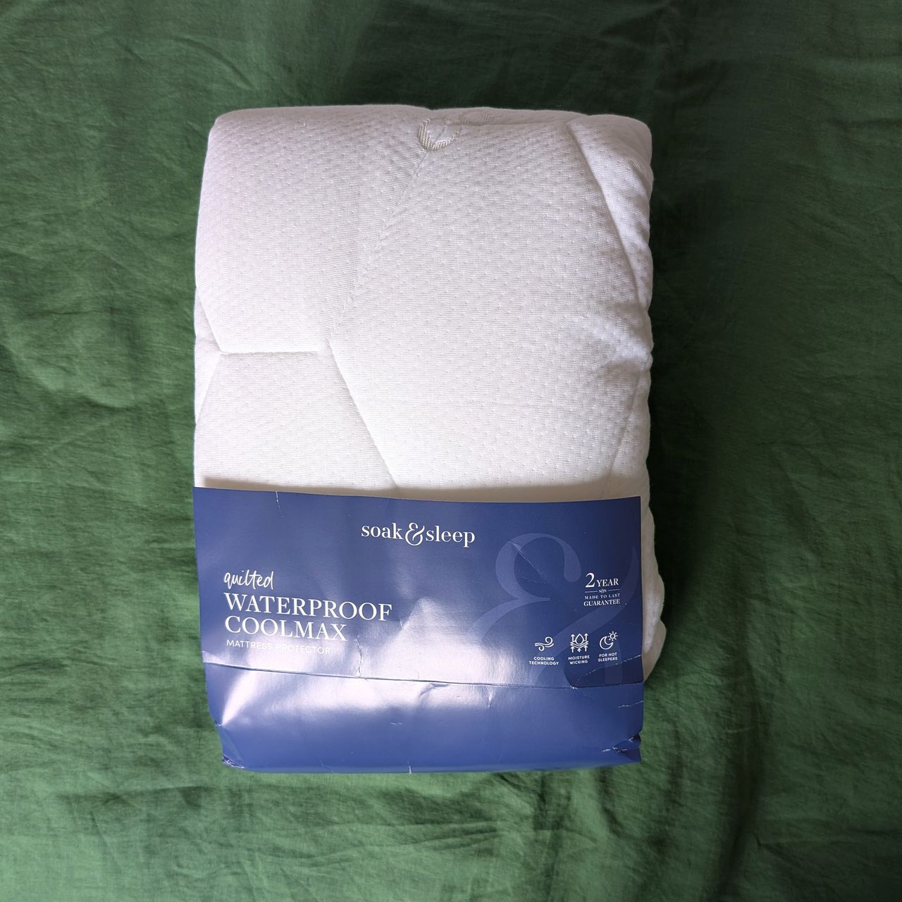 The soak and sleep mattress protector is folded up with a blue label from the original packaging