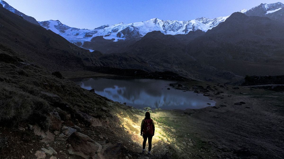 Hiker watching sunrise over snowy mountains and lake 