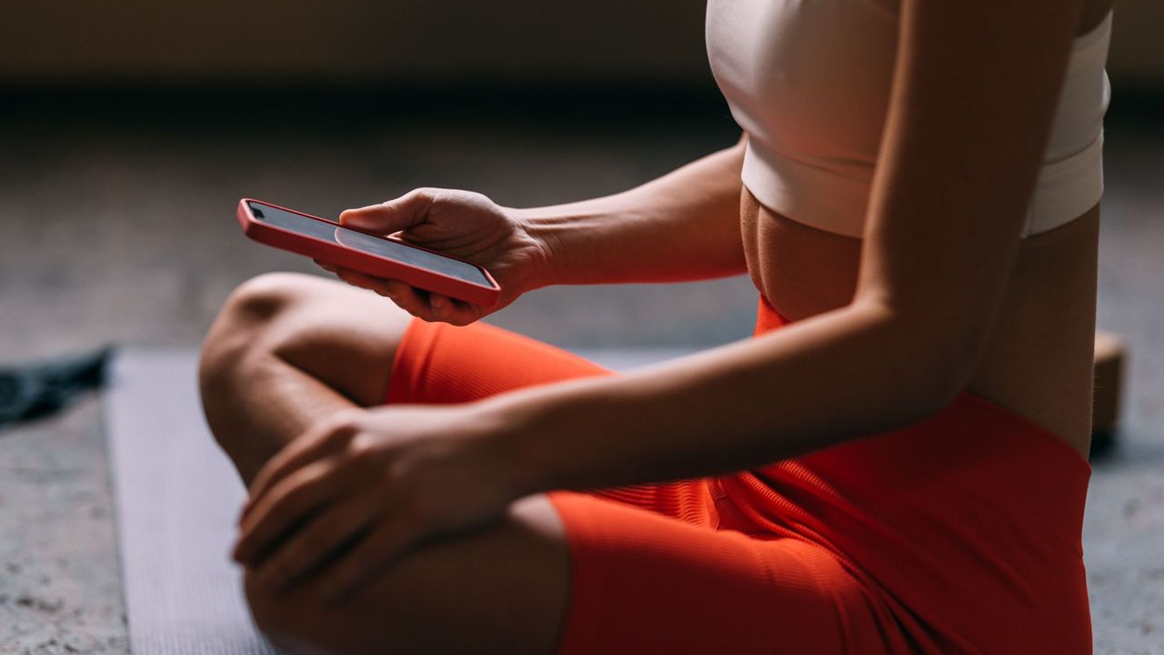 A woman sat cross legged on the floor looking at her phone