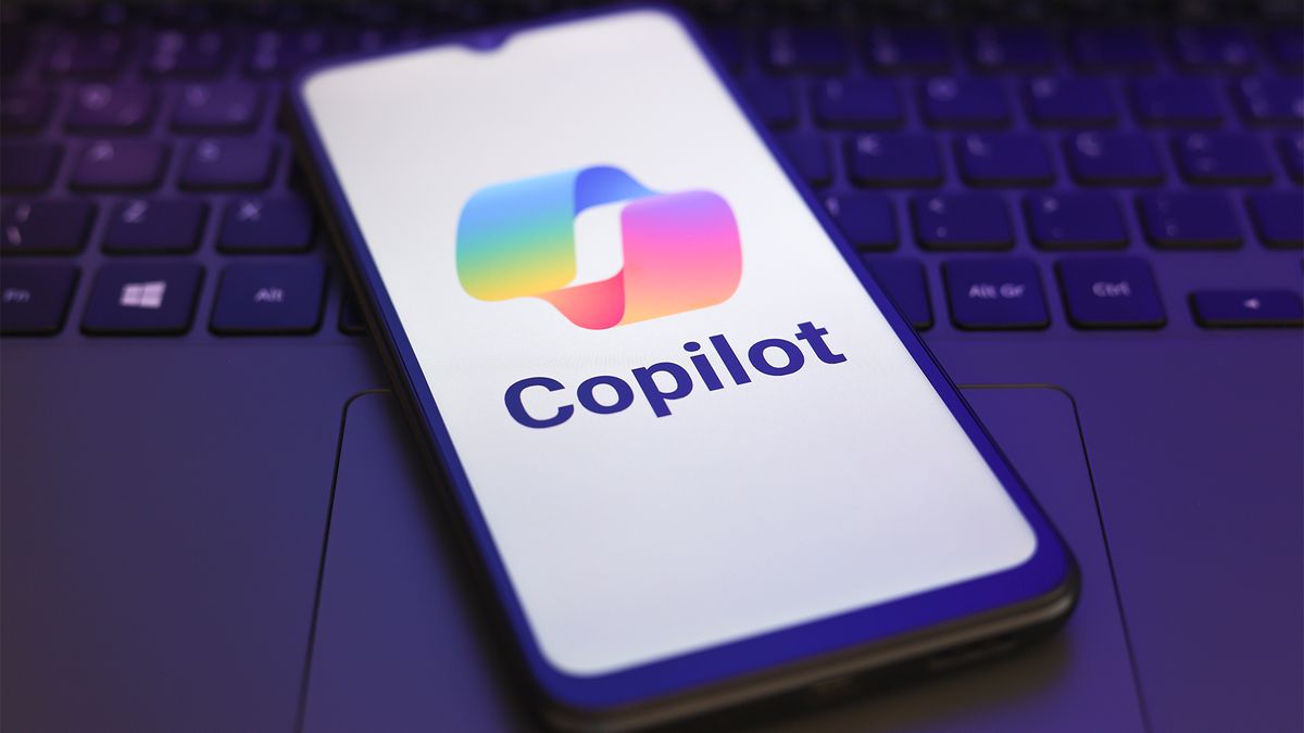 Microsoft Copilot logo and branding pictured on a smartphone screen, with smartphone placed on top of a laptop keyboard.