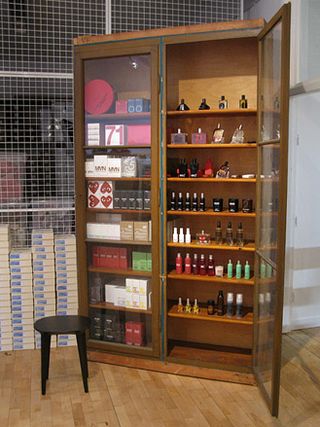 Wooden cabinet displaying perfumes, with one glass-fronted door open