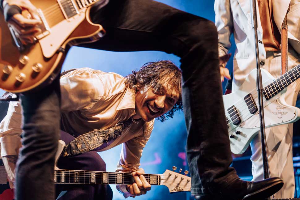 Justin Hawkins onstage, peering through Dan Hawkins' legs